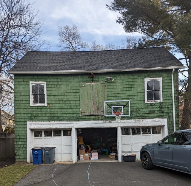 Le Backyard Barn before renovation: green shingle siding, a boarded hay door and two garage bays in Westfield, NJ