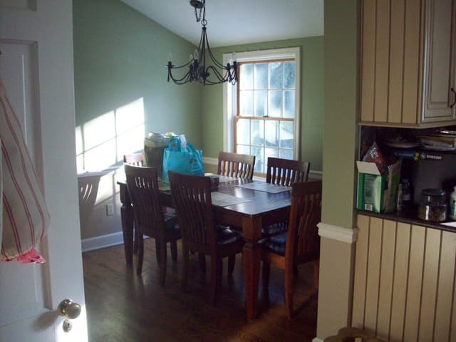 The dining area of a Westfield, NJ home before renovation, with green walls, an iron chandelier and a dark wood table against the beadboard