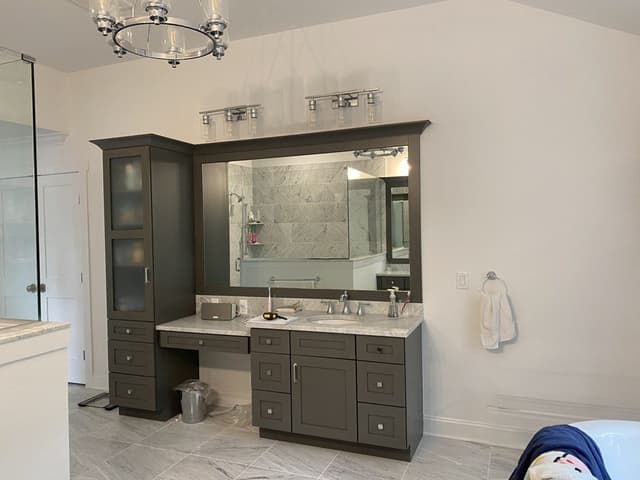 The double vanity of a Westfield, NJ new-construction home before renovation, gray-stained with a seated makeup station between the basins