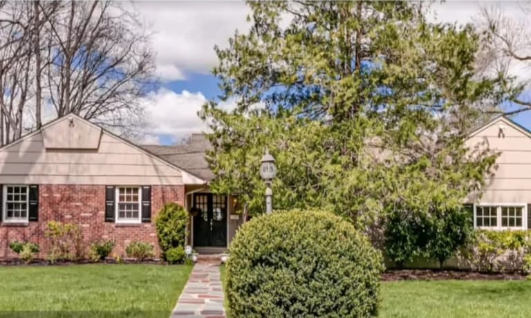 The Westfield, NJ home before renovation: a single-storey ranch in red brick and pale clapboard with black shutters and a low hipped roof, behind a mature evergreen