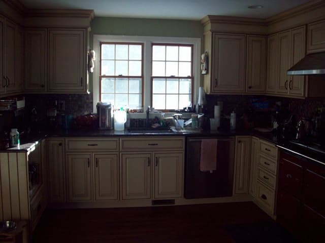 The kitchen of a Westfield, NJ home before renovation, with glazed cream cabinetry, dark counters and a red range against a mosaic backsplash