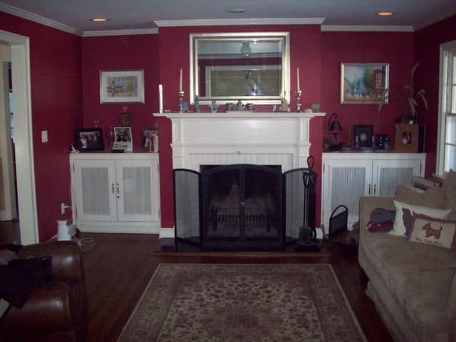 The living room of a Westfield, NJ home before renovation, with deep red walls either side of a white fireplace and built-in cabinets