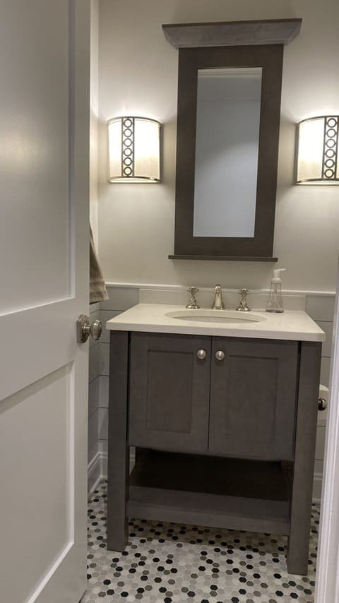 The powder room of a Westfield, NJ new-construction home before renovation, with a gray-stained vanity, a framed mirror and a pebble mosaic floor