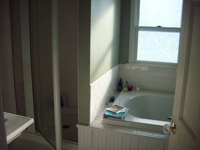 The primary bathroom of a Westfield, NJ home before renovation, with a corner drop-in tub in a tiled deck beside a glass shower