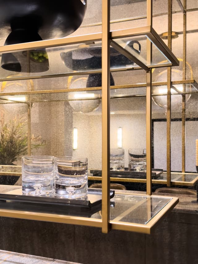 Brass-framed hanging bar shelving with cut glassware above a dark stone counter and an antique mirror wall in a luxury Summit, NJ home