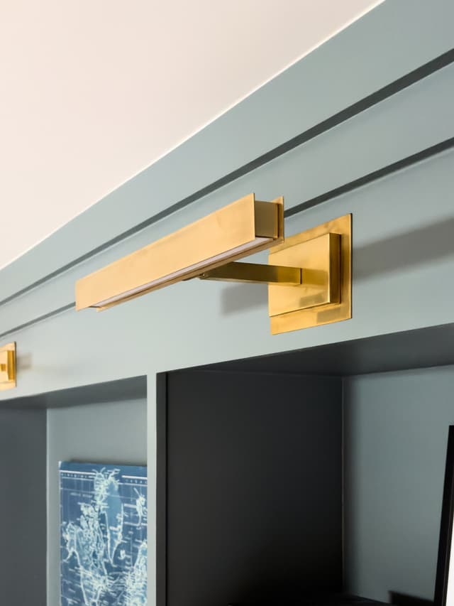 Brass picture light on pale blue-green panelled millwork above framed art in a luxury Summit, NJ home renovation