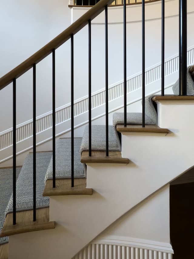 Curved staircase with slim iron balusters, an oak handrail and a patterned runner in a luxury Summit, NJ home renovation by Michael Robert Construction
