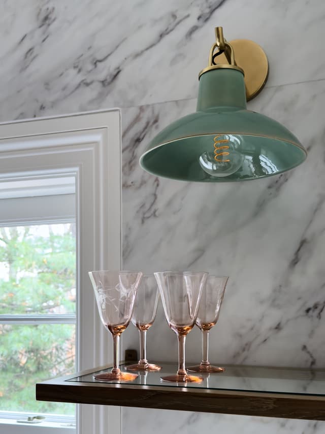 Green enamel sconce on a marble bar wall above a walnut shelf in a luxury Summit, NJ home renovation