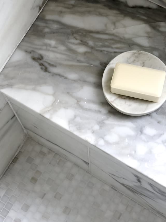 Mitred marble shower bench above a mosaic tile floor in a luxury Summit, NJ bathroom renovation by Michael Robert Construction