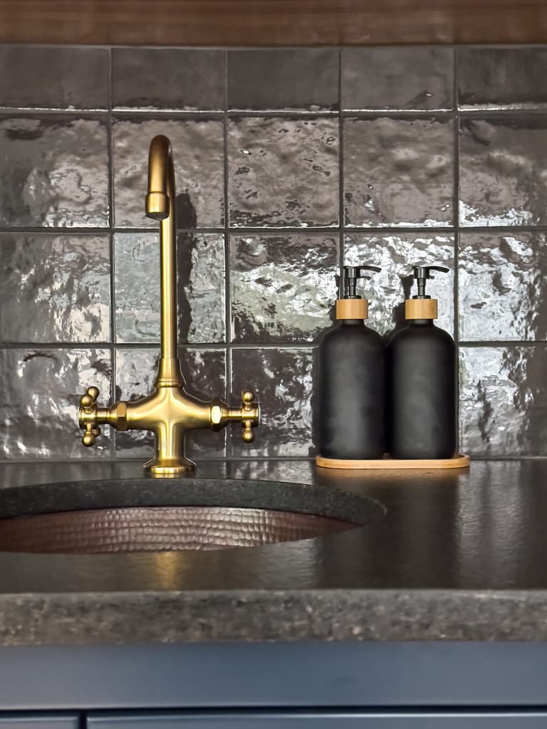 Unlacquered brass bridge tap over a hammered copper bar sink against a smoke-glazed tile backsplash and soapstone counter at a Westfield, NJ renovation and addition by Michael Robert Construction