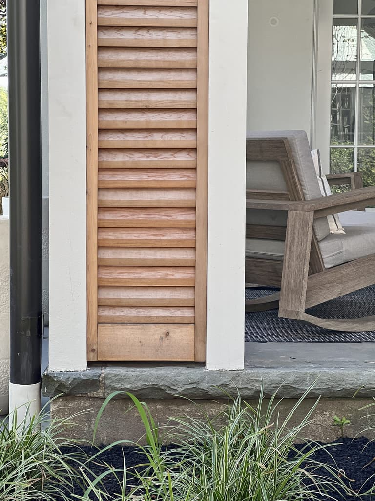 Cedar louvered shutter against white siding beside a stone step and ornamental grasses at a Westfield, NJ renovation and addition by Michael Robert Construction