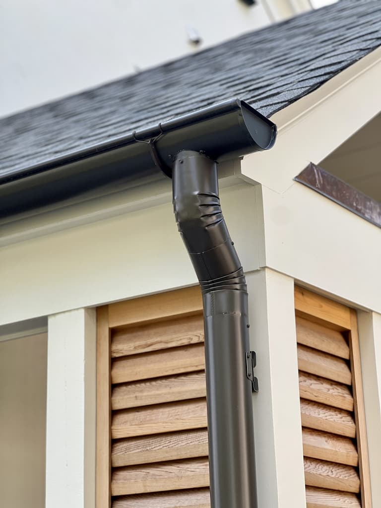 Half-round bronze gutter and round downspout turning the corner of a roof above cedar louvered shutters at a Westfield, NJ renovation and addition by Michael Robert Construction