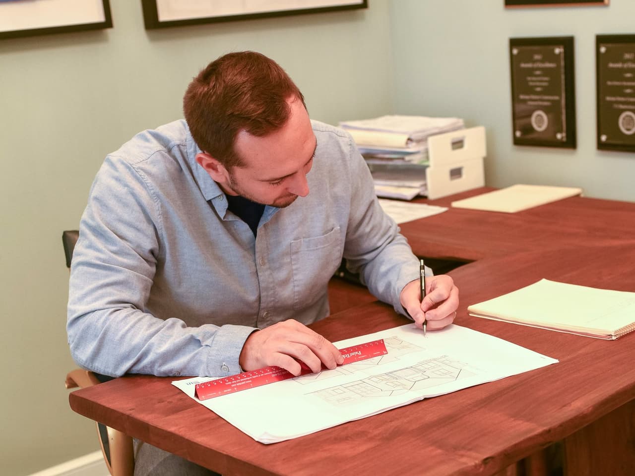 Mike Mroz marking up an architectural elevation with a scale rule at his desk in the Michael Robert Construction office in Westfield, NJ