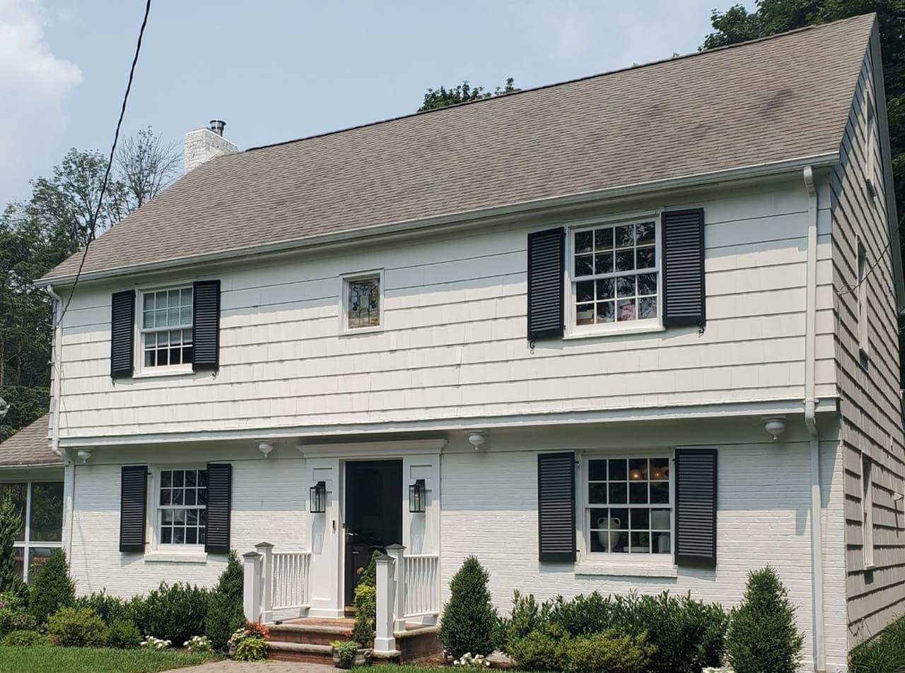The Summit, NJ home before renovation: white clapboard over painted brick, black shutters and a small flat-hooded entry, with no dormers across the front roof
