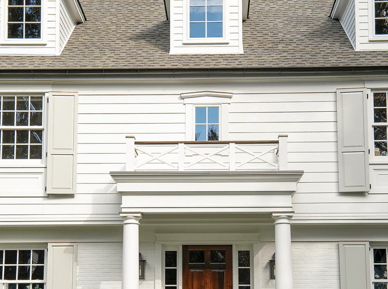 Front elevation of a Summit, NJ exterior remodel, with a pedimented portico over a wood door and sidelights, dormers above and clipped boxwood either side