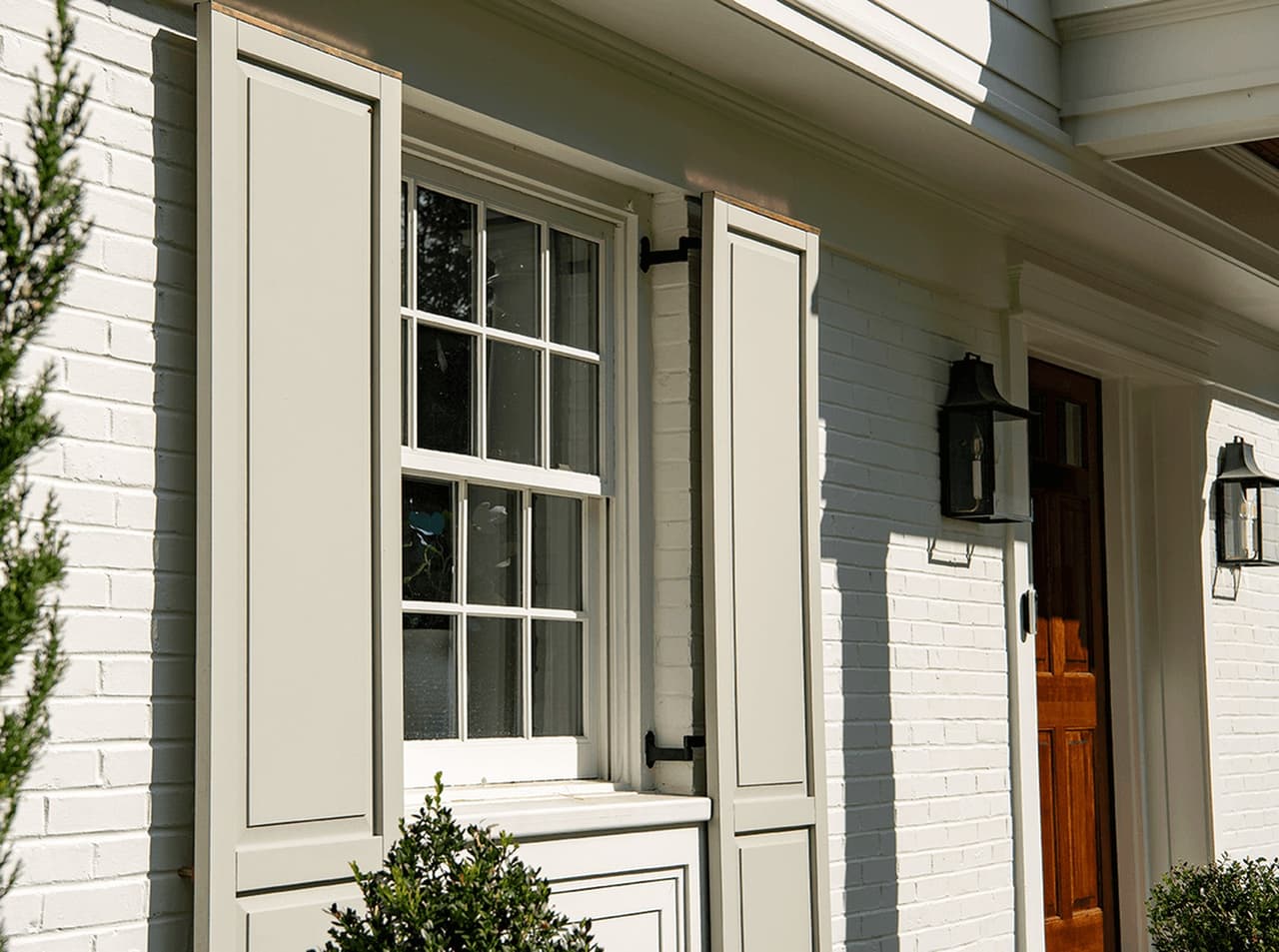 Custom louvered shutters and a lantern beside the door of a Summit, NJ exterior renovation, seen at an angle along the painted brick