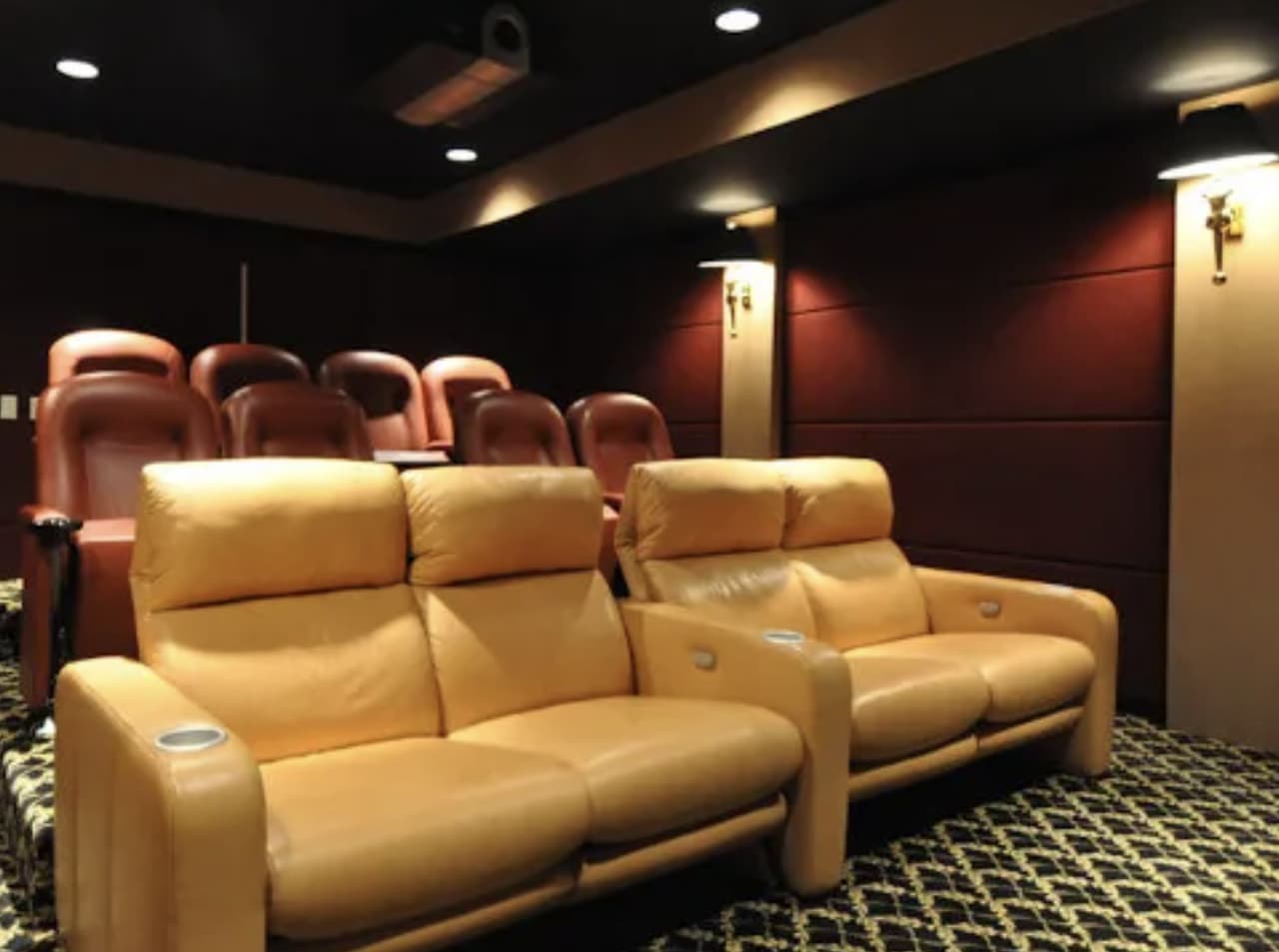 The lower level of a luxury Summit, NJ home before renovation, a closed-off theater with tiered tan leather recliners and no bar or lounge