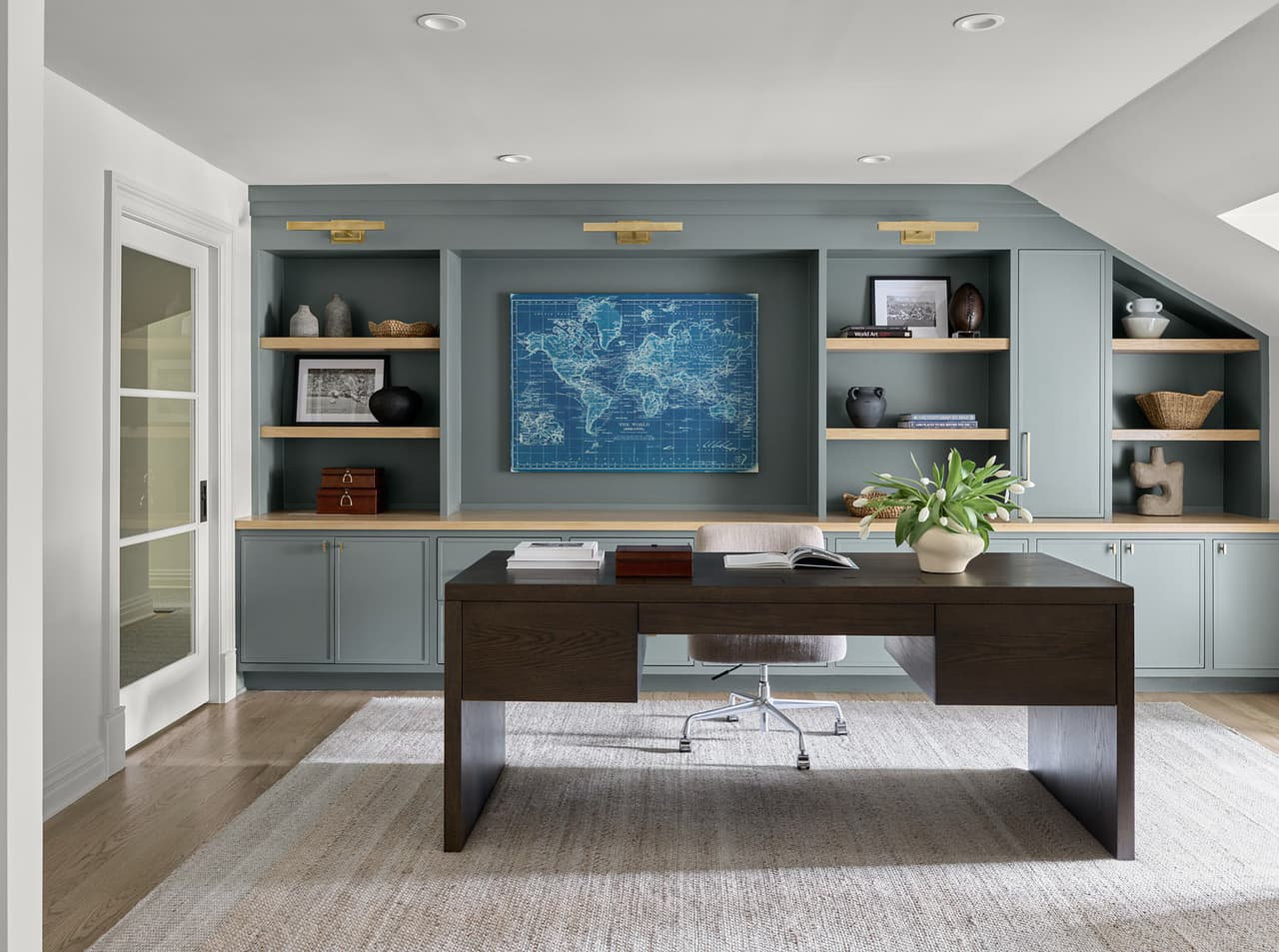 The completed home office in a luxury Summit, NJ renovation, with pale blue-green built-ins framing a mounted map above a dark wood desk under a sloped ceiling