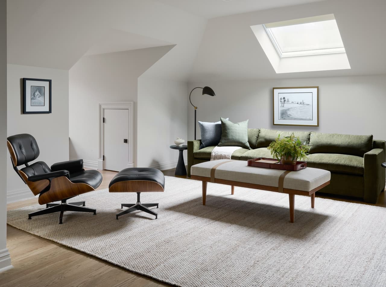 The completed seating area of a luxury Summit, NJ home office, under a sloped ceiling with a skylight, with a leather lounge chair, a green sofa and a bench on a pale rug