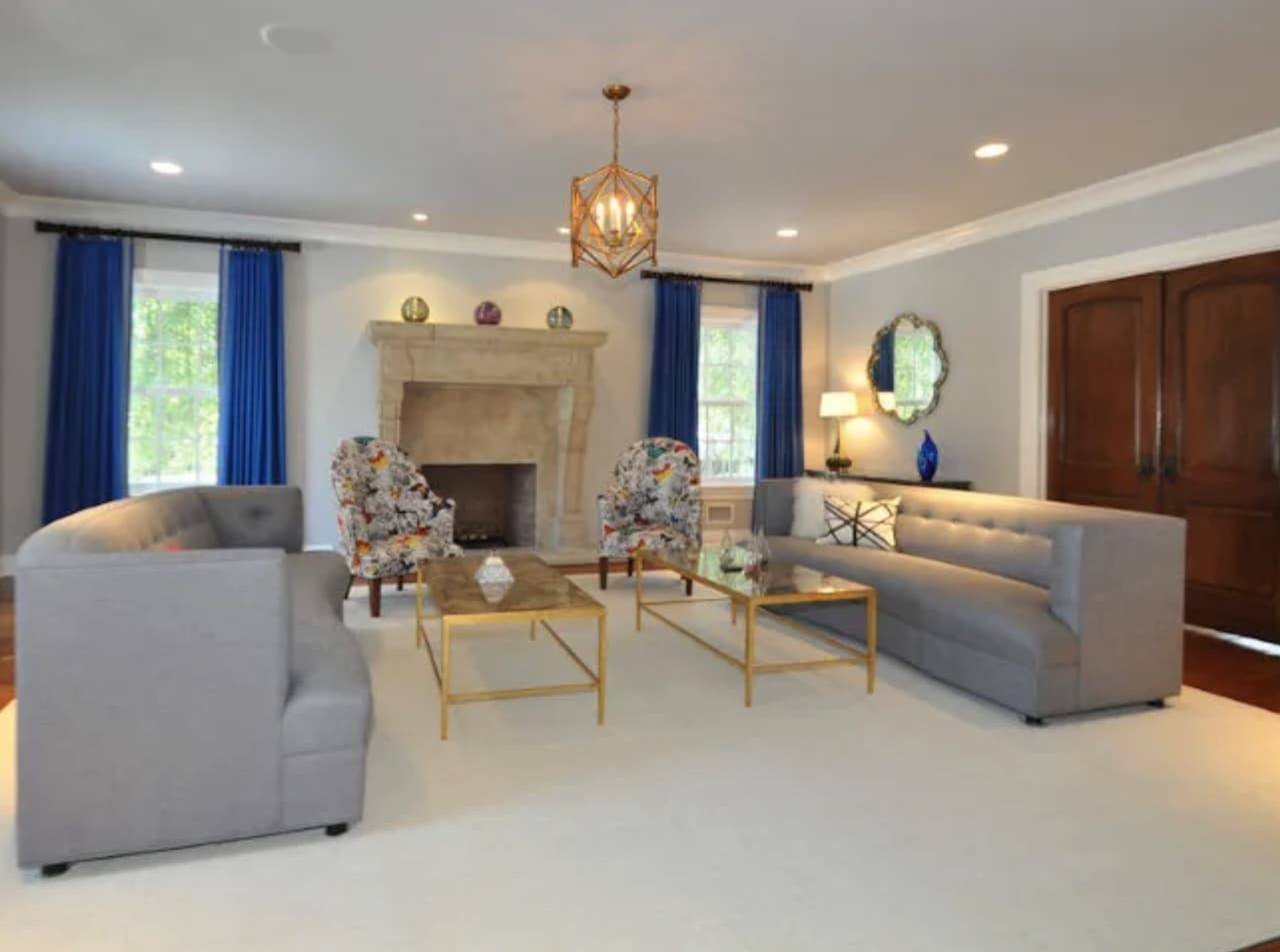 The formal living room of a luxury Summit, NJ home before renovation, with gray sofas, blue drapery and a plain painted fireplace wall