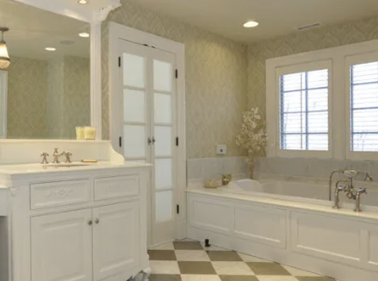 The primary bathroom of a luxury Summit, NJ home before renovation, with a white vanity, a drop-in tub under the window and a checkerboard tile floor