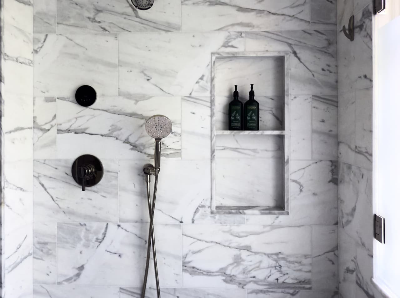 Bookmatched marble shower with a recessed niche and matte black fittings in a luxury Summit, NJ primary bathroom renovation