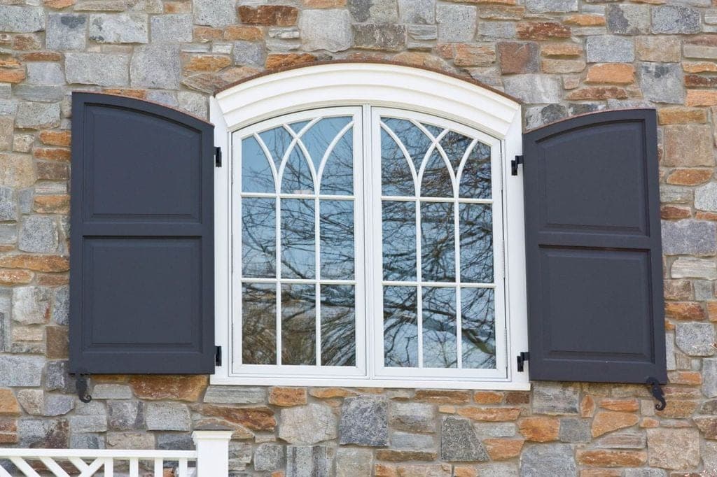 Arched window with Gothic muntins and dark shutters set into the fieldstone wall of a Westfield, NJ cape renovation