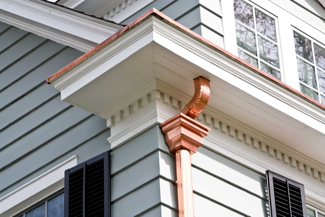 Copper leader head and bracketed cornice return where the roofline turns at a Westfield, NJ home, against gray clapboard