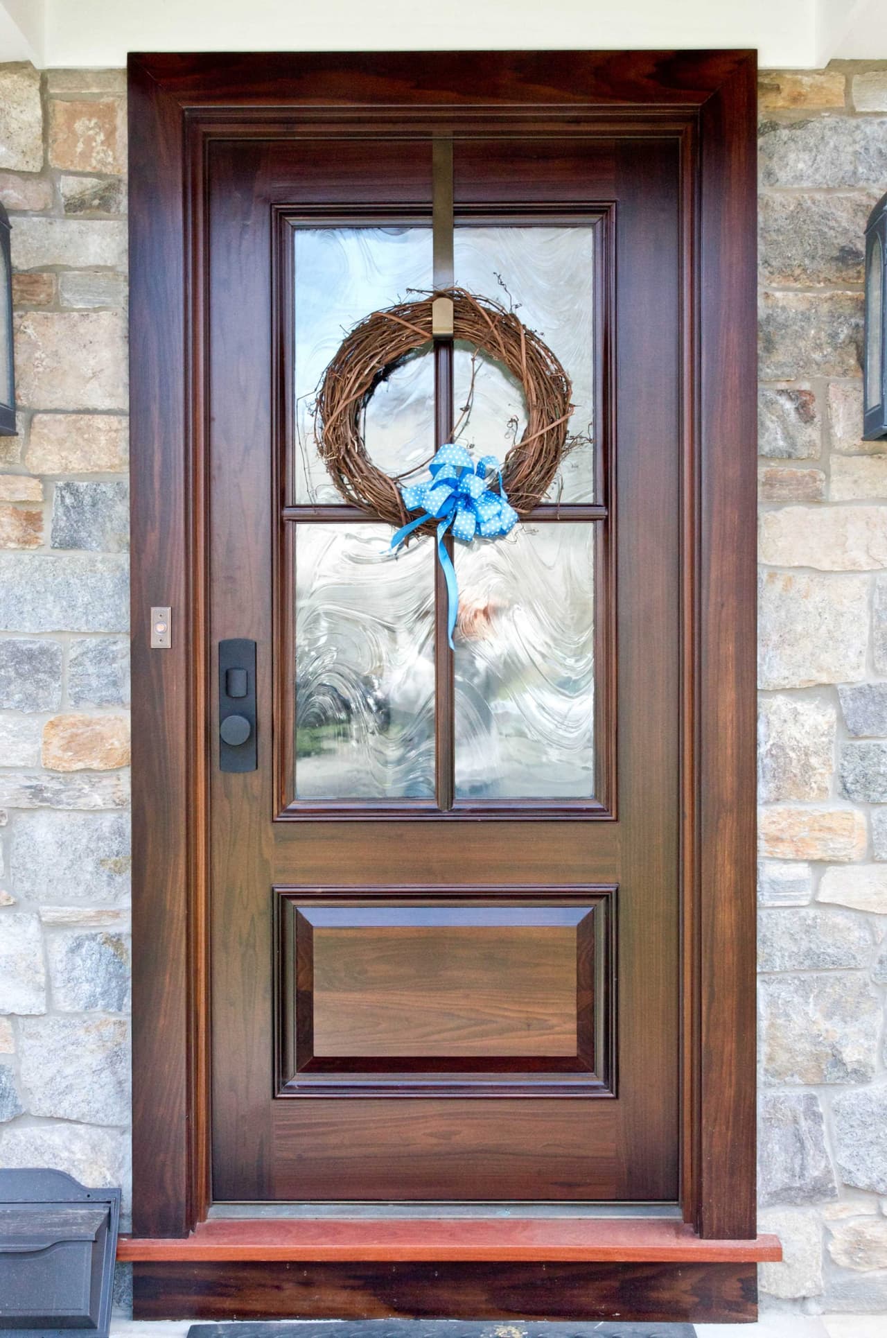 Stained mahogany front door with leaded glass and a wreath, set into a stone surround