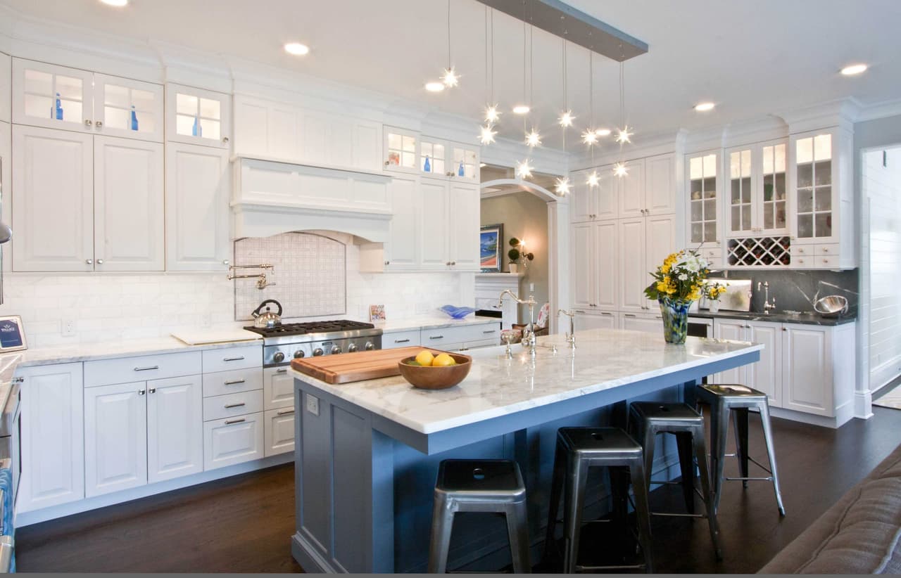 Kitchen with white cabinetry, a gray island with a butcher-block end, metal stools and glass-front uppers