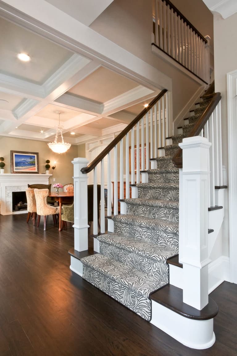 Stair with a patterned runner, square newel posts and a coffered ceiling above the room beyond
