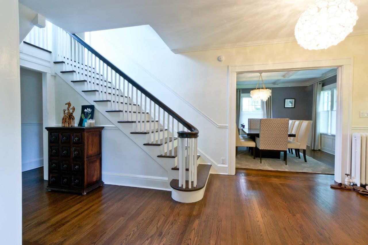 Foyer of a Westfield, NJ renovation, with a white painted stair and dark handrail, a wide-plank floor and the dining room through the opening