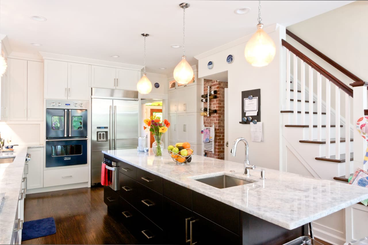 Kitchen looking toward the stair, with a dark island, undermount sink and stainless wall ovens