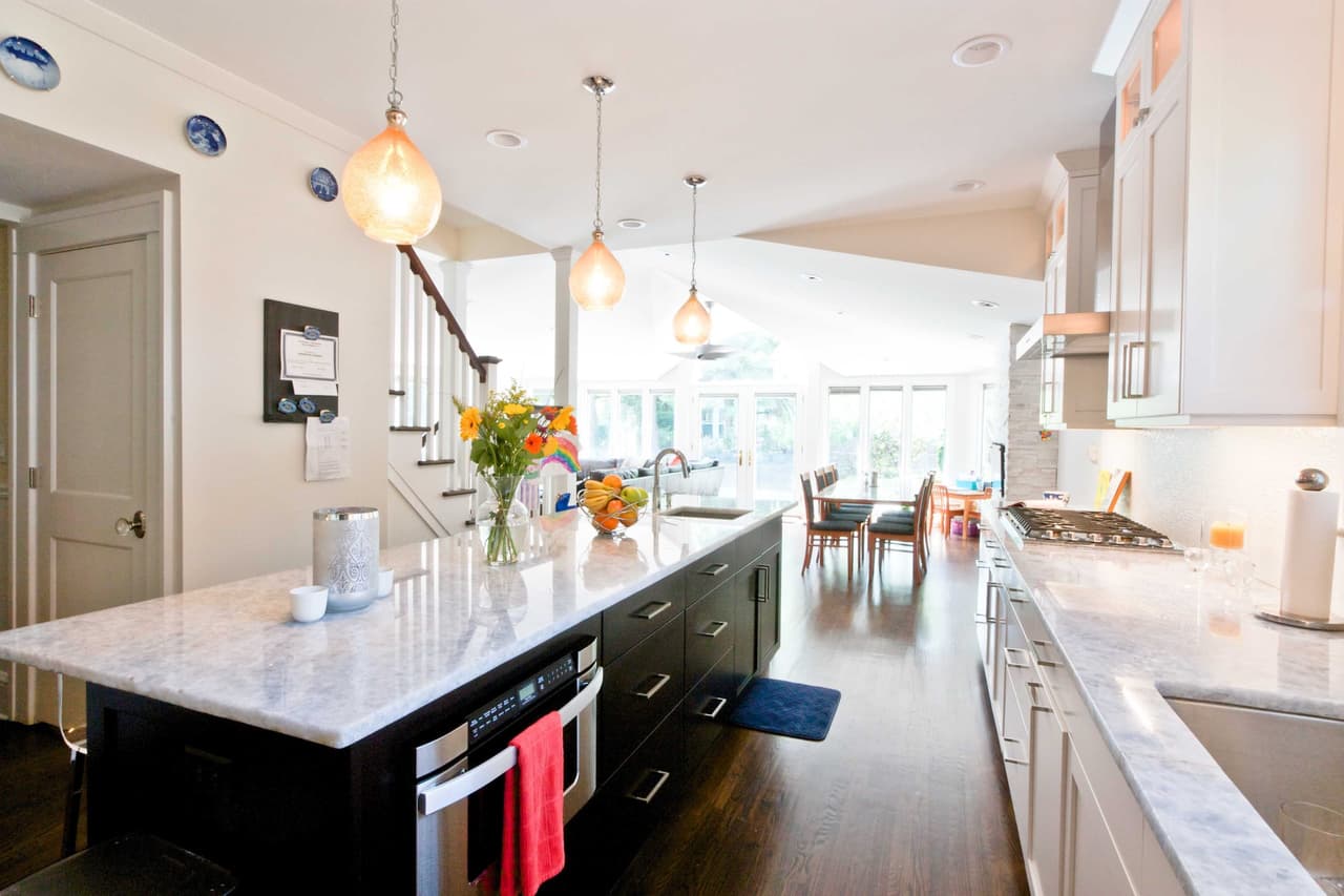Kitchen island in marble with glass globe pendants above, open to a dining area at the far end