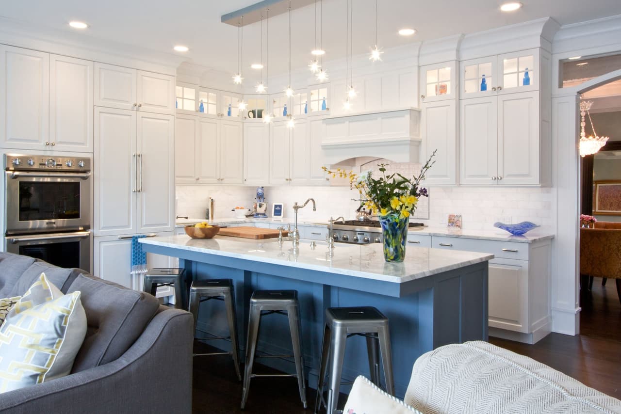 Kitchen open to the family room, with a blue island, counter stools and a wall of glass-front cabinets
