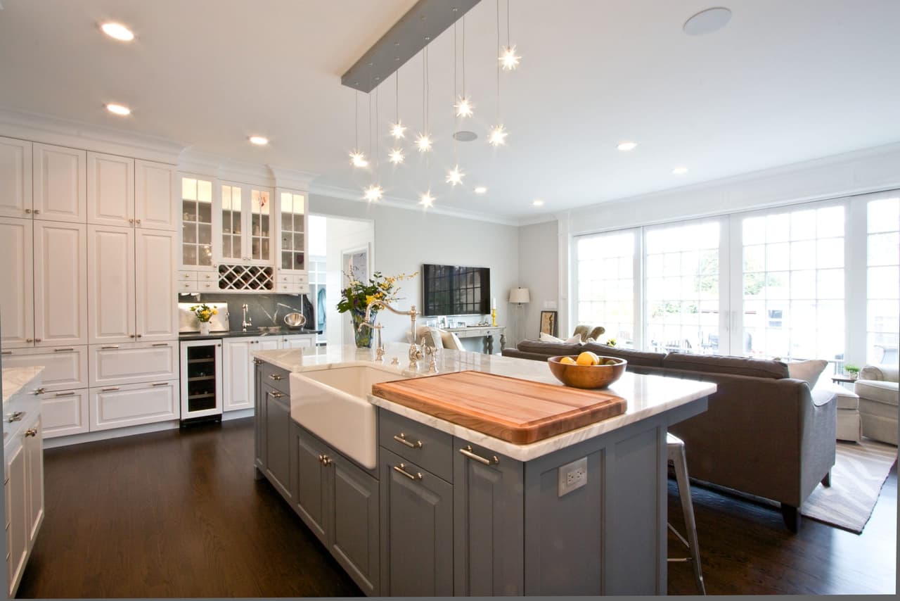 Kitchen island with a farmhouse sink and butcher-block end, beside a sofa and a bank of windows