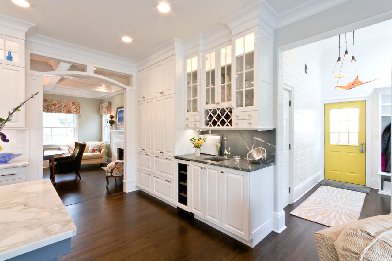 Butler's pantry between the kitchen and hall of a Westfield, NJ cape renovation, with glass-front cabinets, a dark counter and a yellow back door at the end