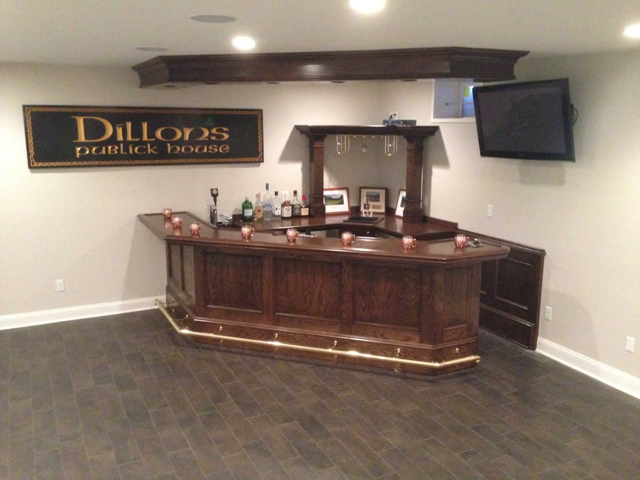 Basement pub with a carved wood bar, a hanging painted sign and a wall-mounted television