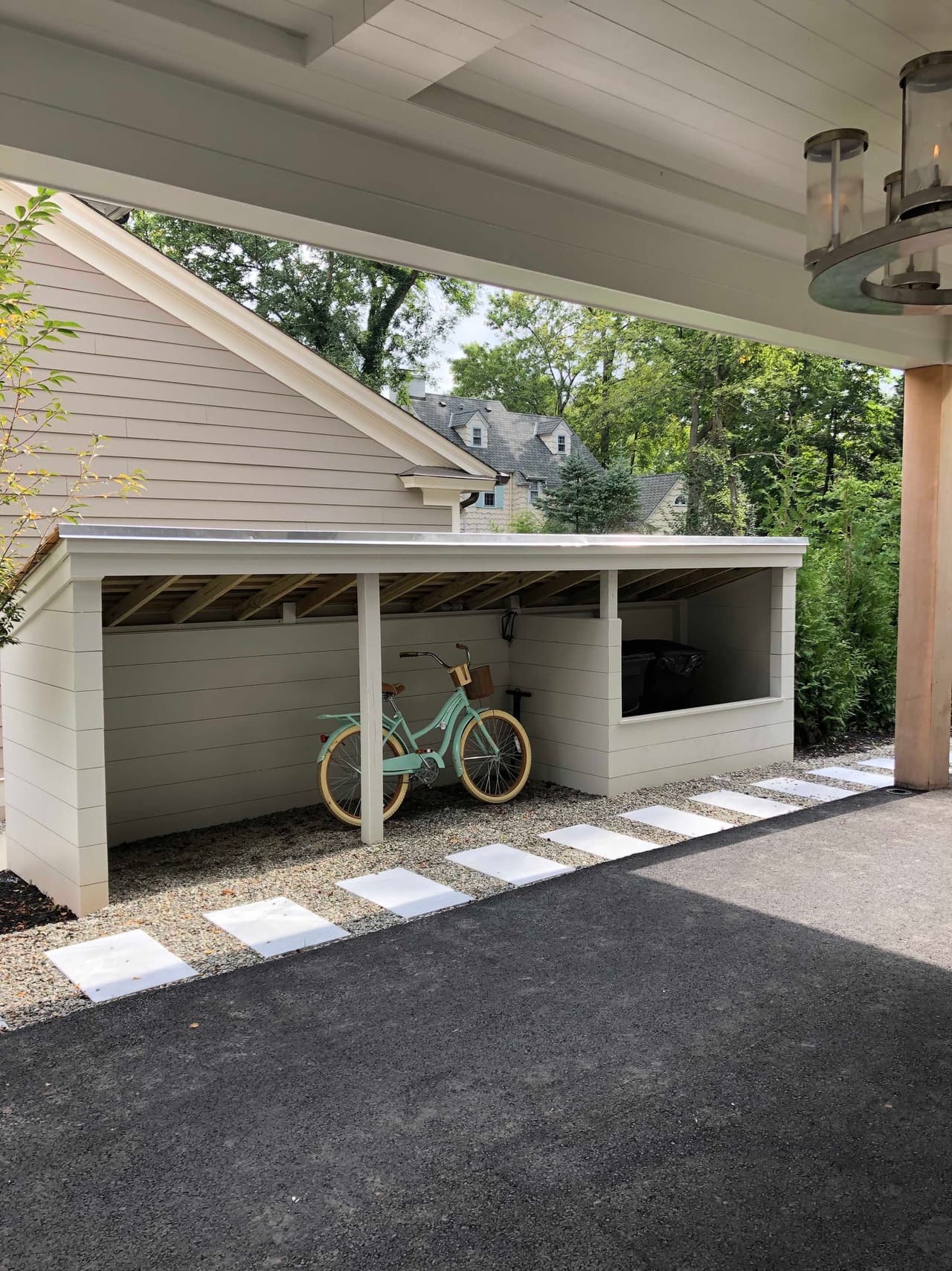 Rear of the garage with a covered bay and a bicycle, beside a paved drive and stepping-stone path