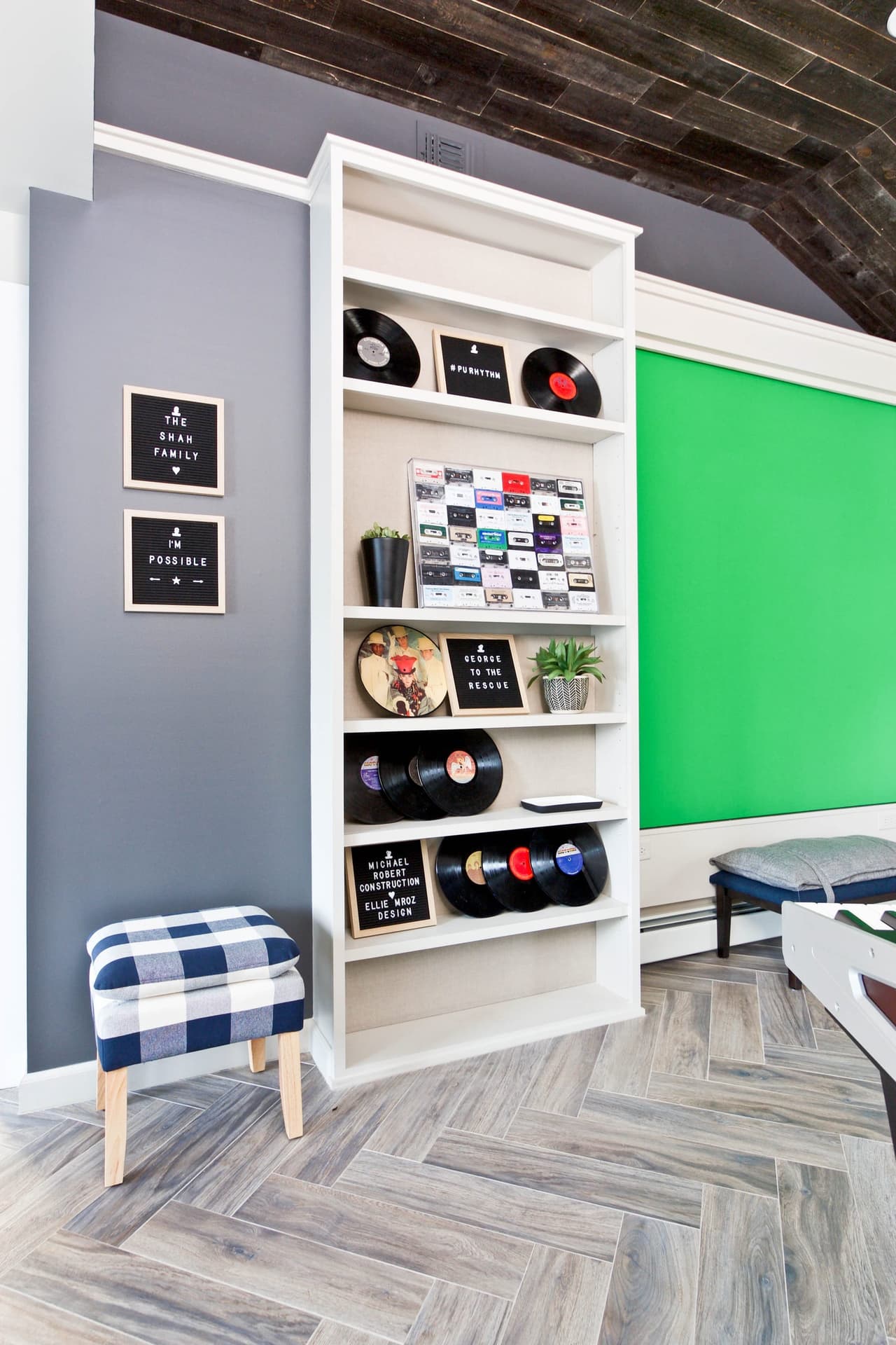 Playroom with a green-painted activity wall, white shelving holding records and a herringbone wood floor