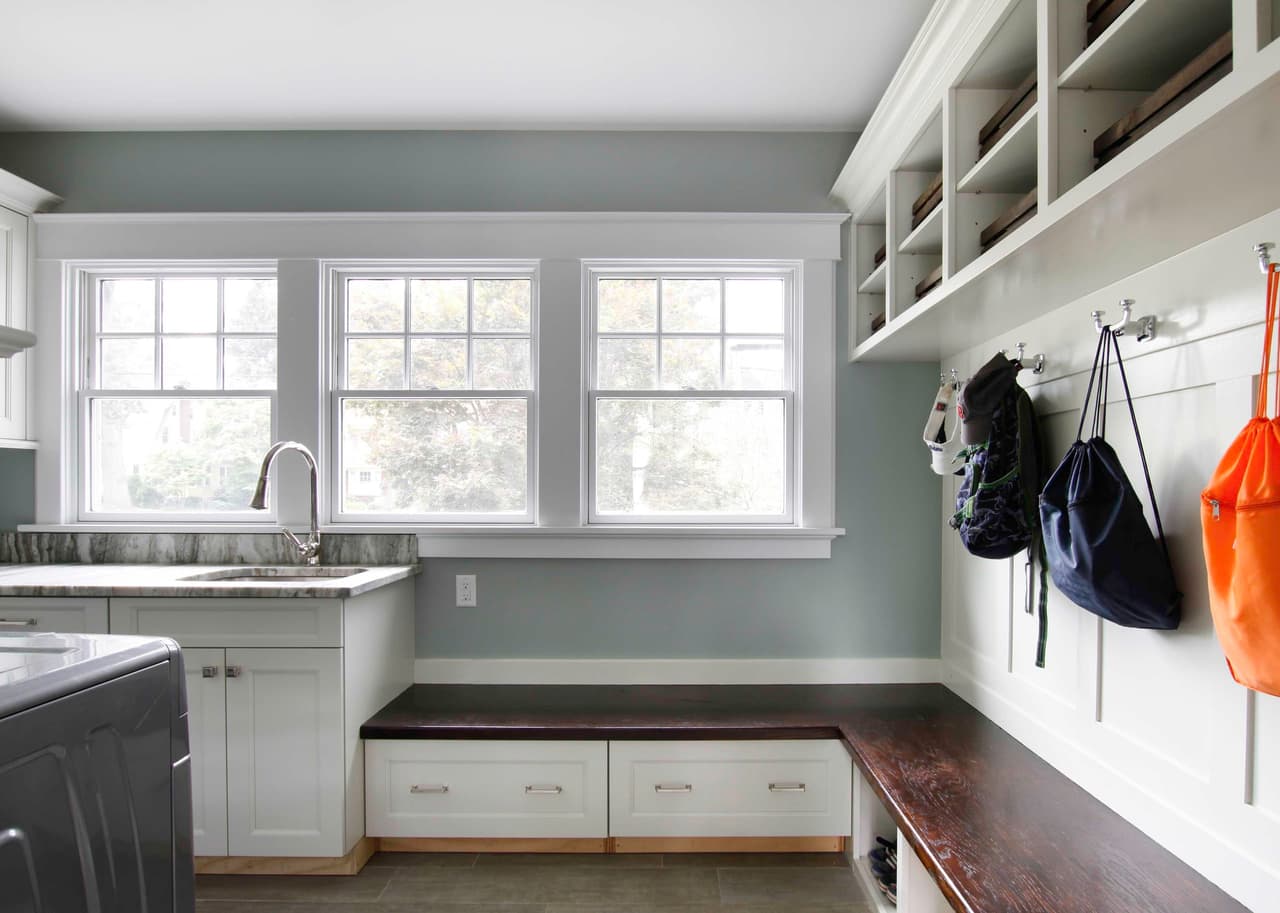 Mudroom with a built-in bench, cubby storage above, coat hooks and a sink under three windows