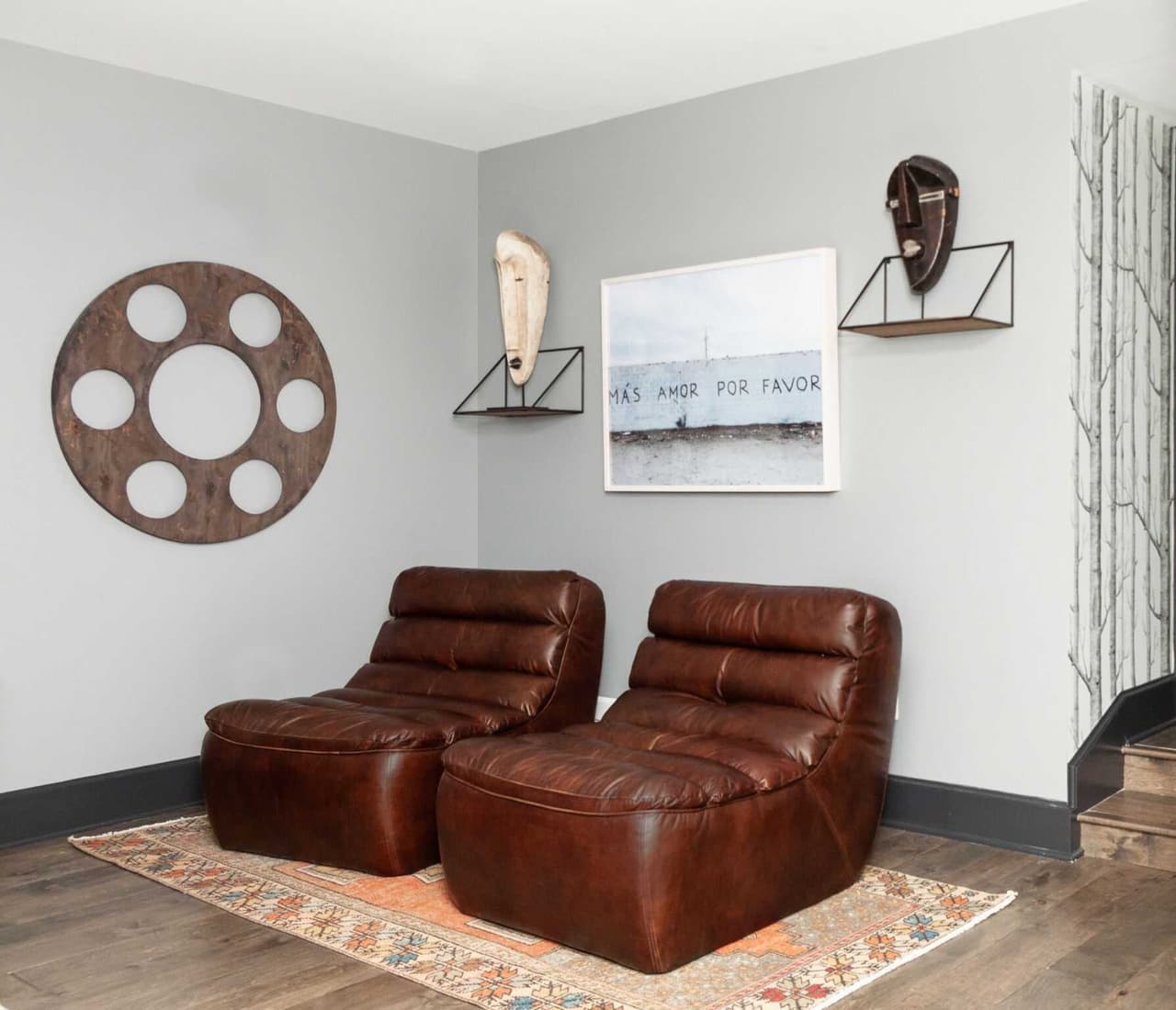 Lower-level sitting area with two brown leather lounge chairs, a round wood wall piece and framed art