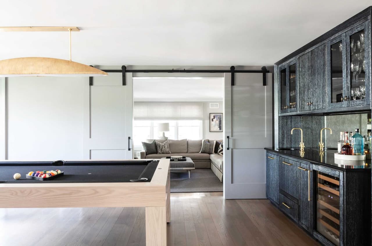 Billiard table and navy bar cabinetry in a Westfield, NJ interior renovation, with a barn door rolled back to the sitting room
