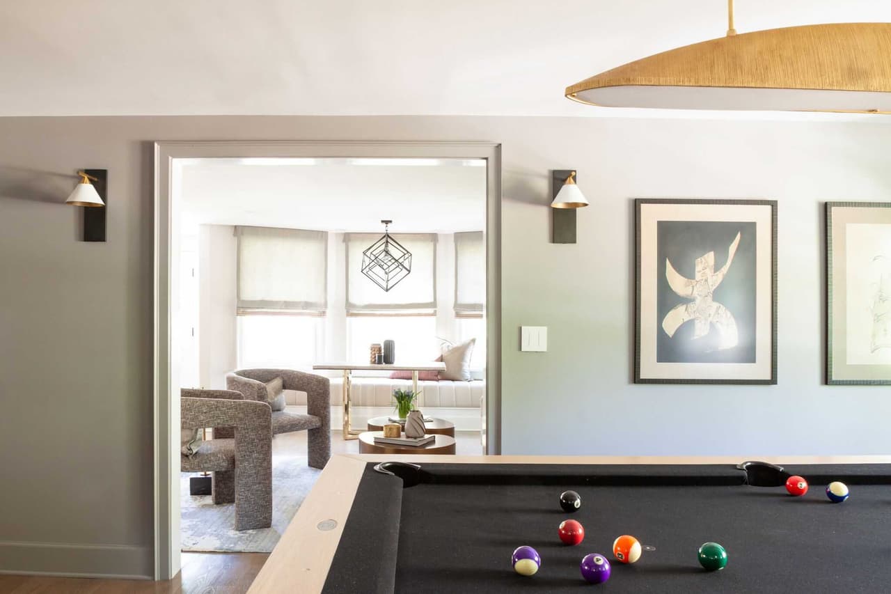 Game room with a pool table and wall sconces, through an arched opening to the kitchen