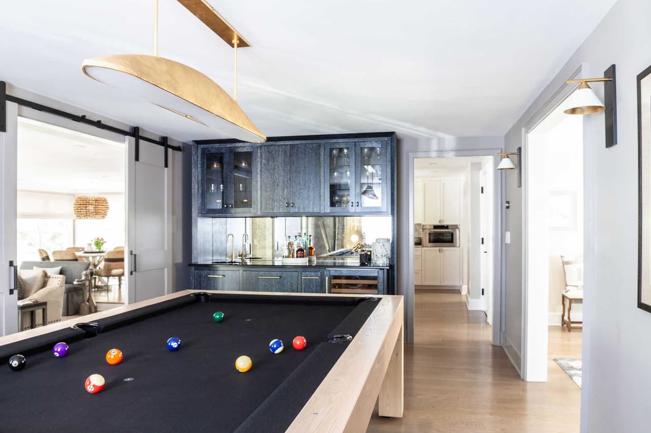 Billiard table in an opened-up Westfield, NJ interior, with a sliding barn door, a navy bar wall behind and a dining room through the far opening