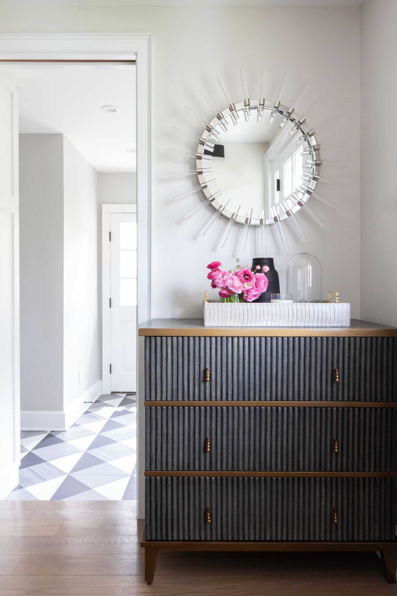 Entry with a sunburst mirror above a fluted dresser, looking through to a checkerboard tile floor