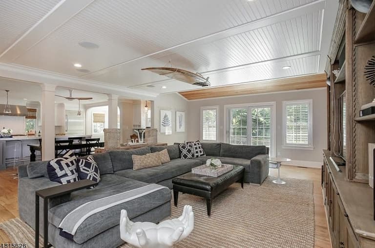 Family room of a classic coastal colonial renovation in Westfield, NJ, with a beadboard ceiling, a gray sectional and the kitchen open beyond