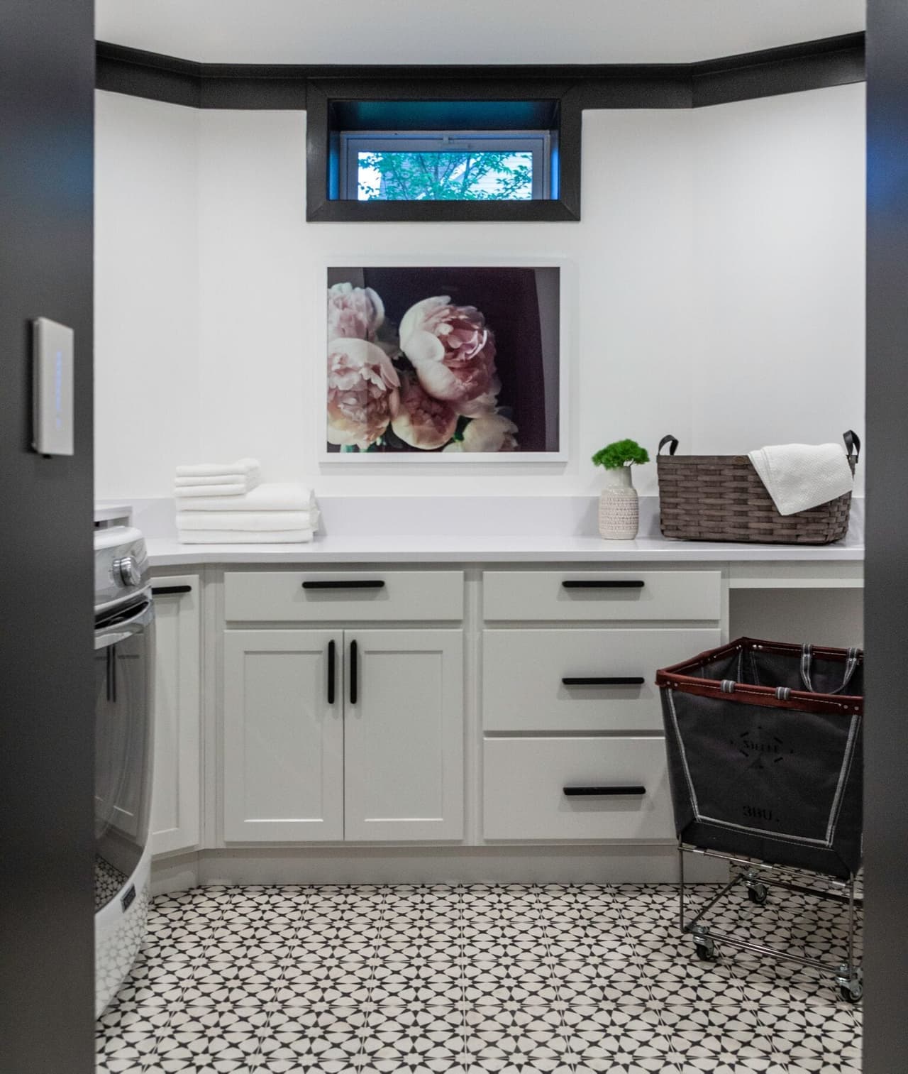 Laundry and mudroom corner in a Westfield, NJ home, with white cabinetry, a folding counter, a framed print and a patterned cement tile floor