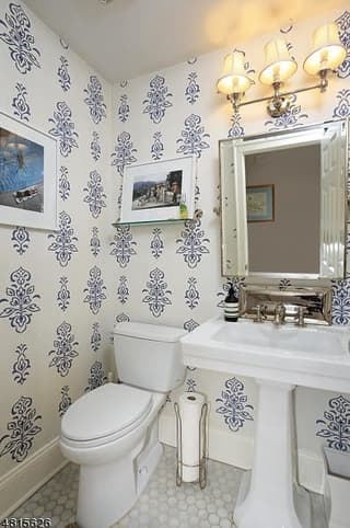 Powder room of a Westfield, NJ coastal colonial renovation, papered in a blue block print, with a pedestal basin and a brass-lit mirror