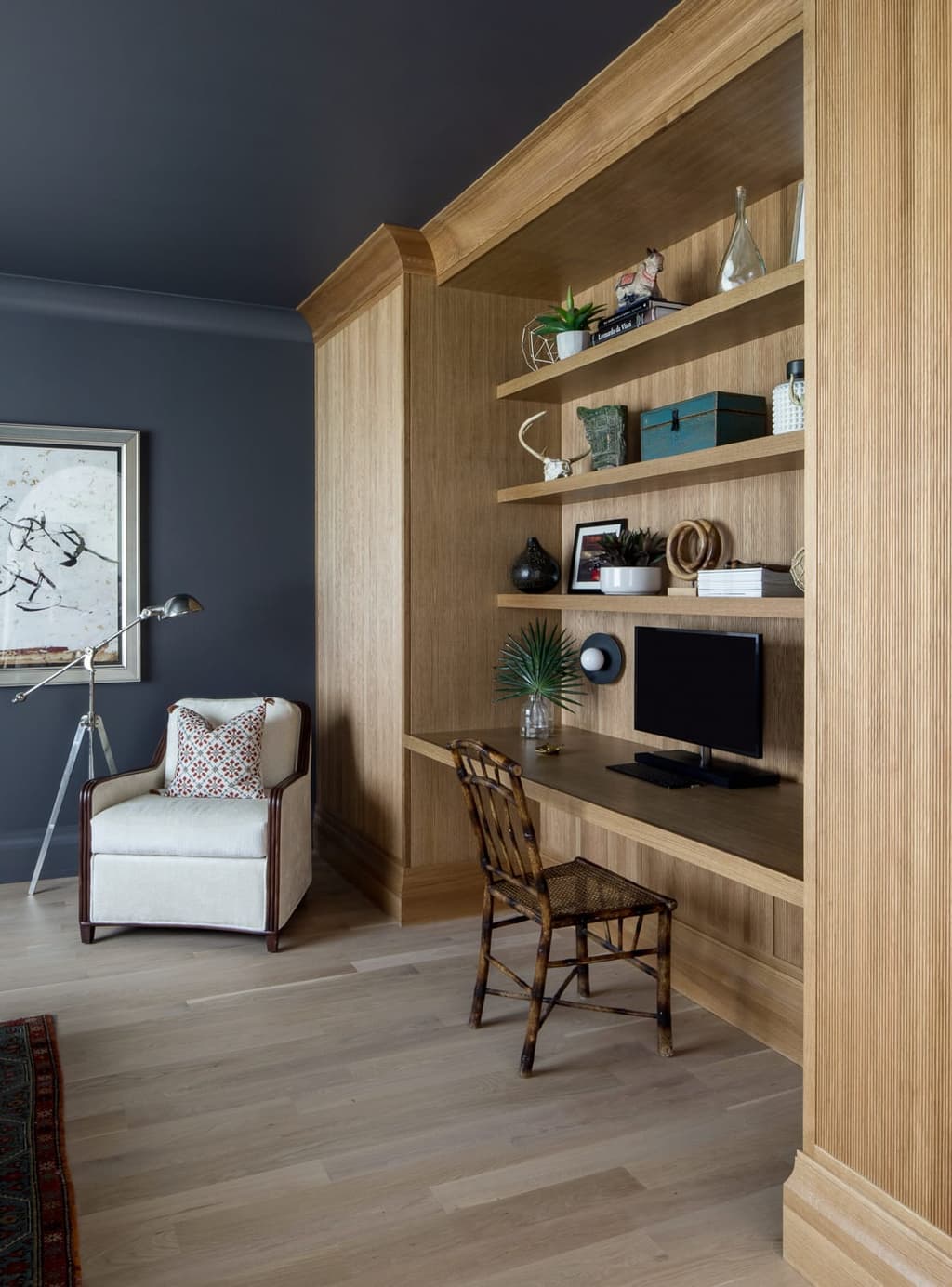 Home office nook lined in white oak, with a built-in desk and floating shelves beside a charcoal wall